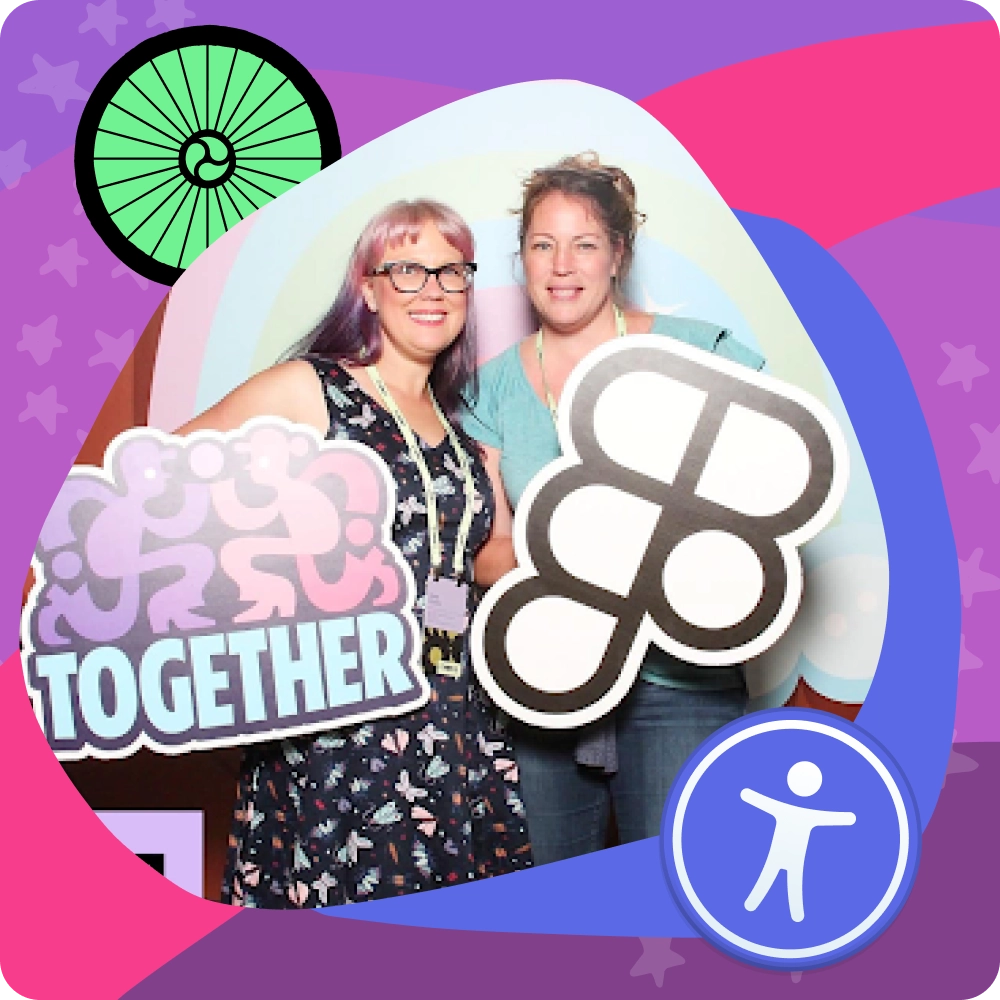 Two women smiling at the Figma Config 2024 design conference. They are standing in front of a colorful backdrop with a rainbow and holding playful Figma-themed props, including one that says 'TOGETHER.' Thea Eaton is on the right wearing a teal shirt, and Keira Dooley is on the left with glasses and a floral dress.